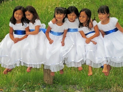 Girls in white dresses with blue satin sashes grass